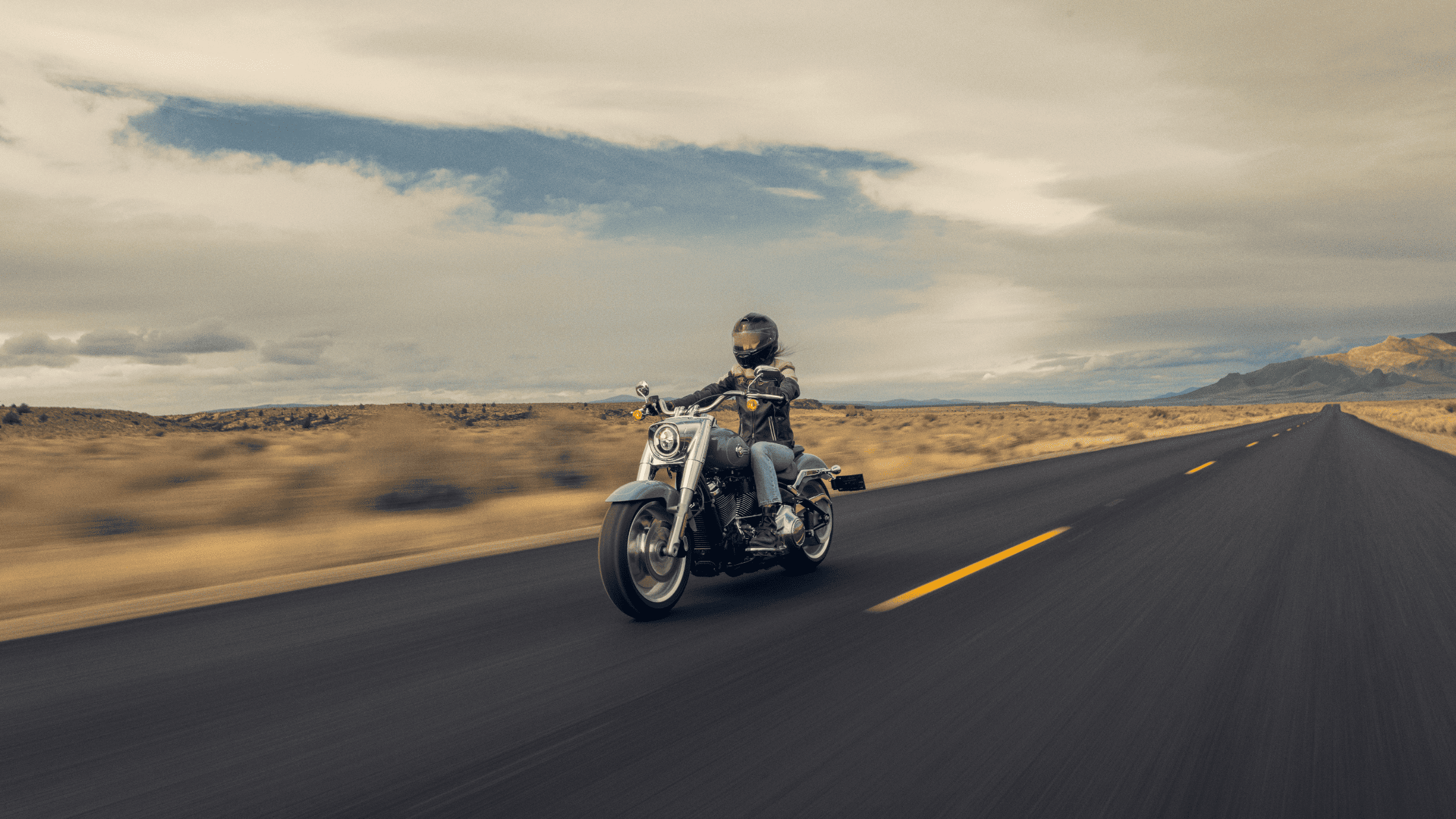 A rider cruising on the 2024 Harley-Davidson® Fat Boy® 114 through open roads near Ormond Beach, FL, showcasing its classic design and powerful performance.