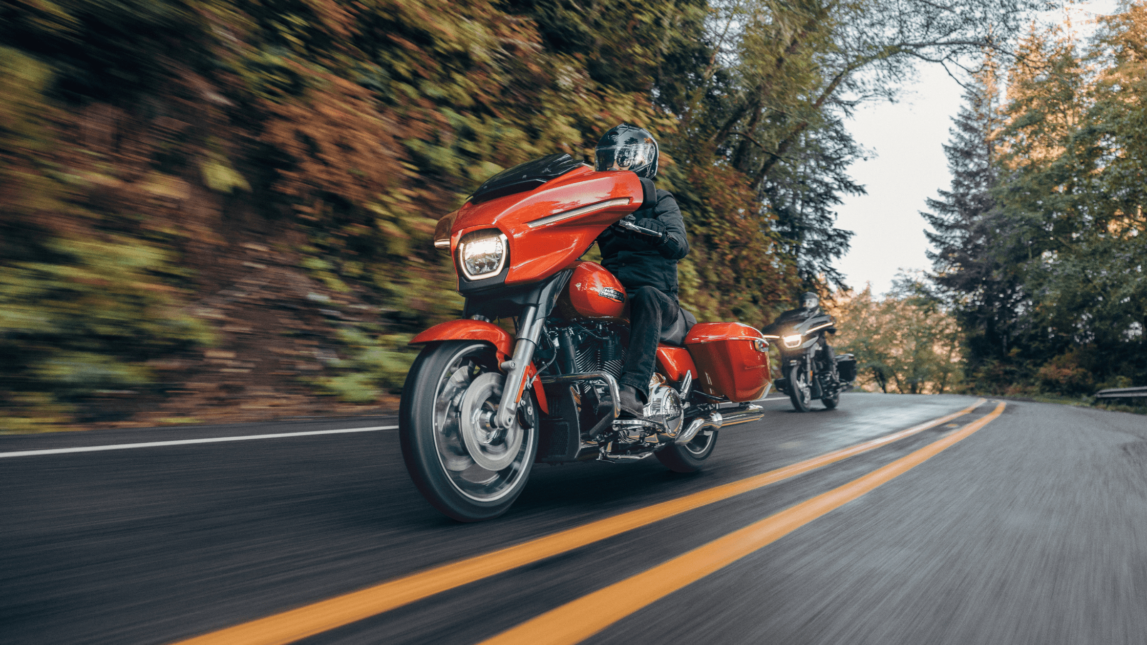 Motorcyclist riding a vibrant red 2024 Harley-Davidson® Street Glide® along a wooded road in Ormond Beach, FL.